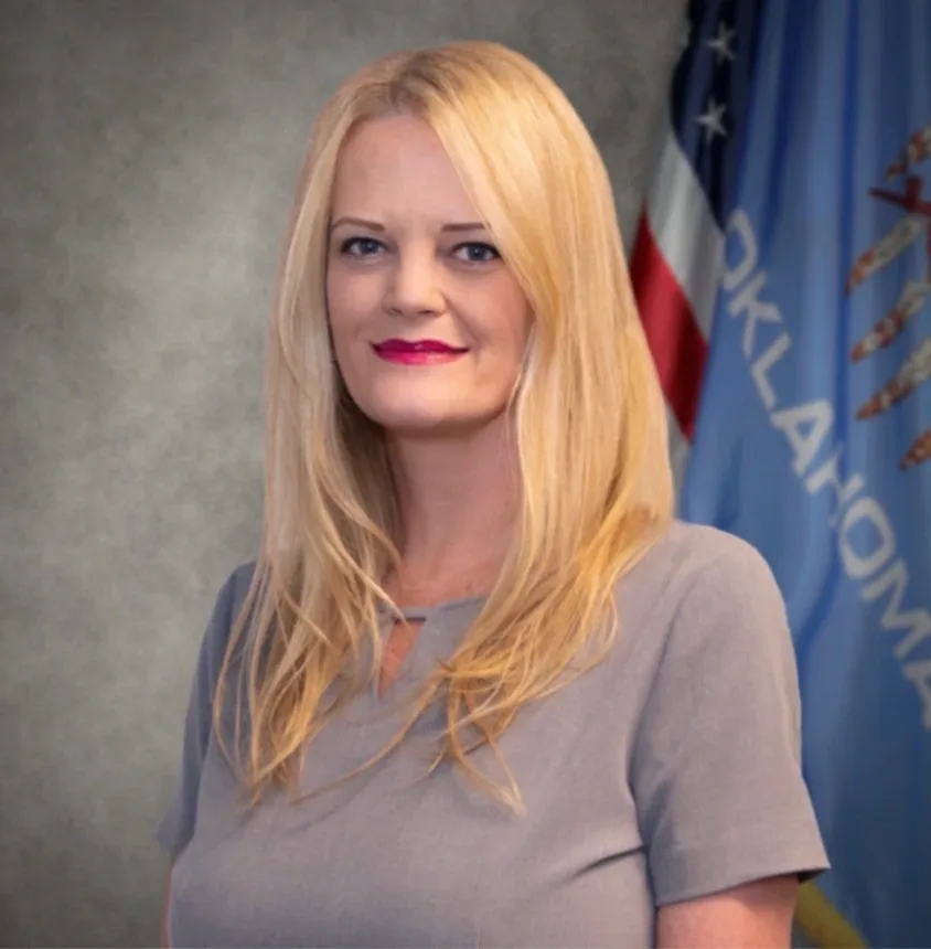 Lesli Bajema, director of statewide procurement strategy at Oklahoma&rsquo;s Office of Management and Enterprise Services, in front of the Oklahoma state flag.